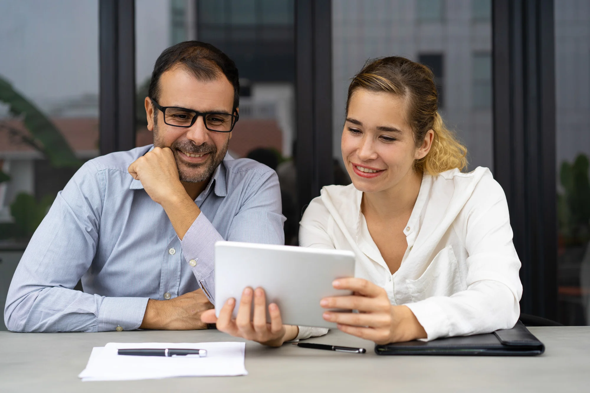 A smiling man and woman sitting at a table reviewing financial data and passive income opportunities on a digital tablet.